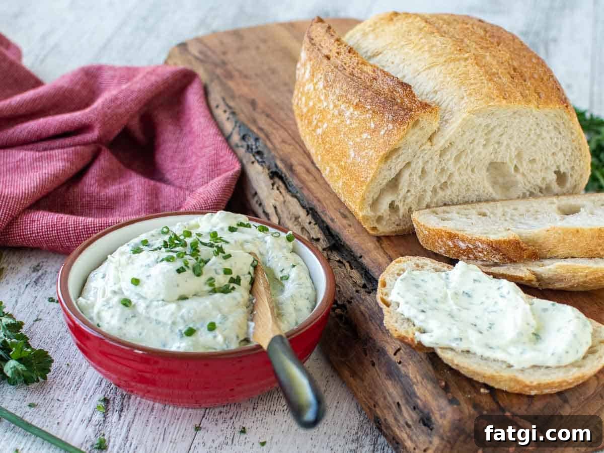 Creamy Homemade Garlic and Herb Cheese Spread Recipe 9 Creamy dip in a red bowl with loaf of partially sliced bread and creamy dip spread on one slice of bread.