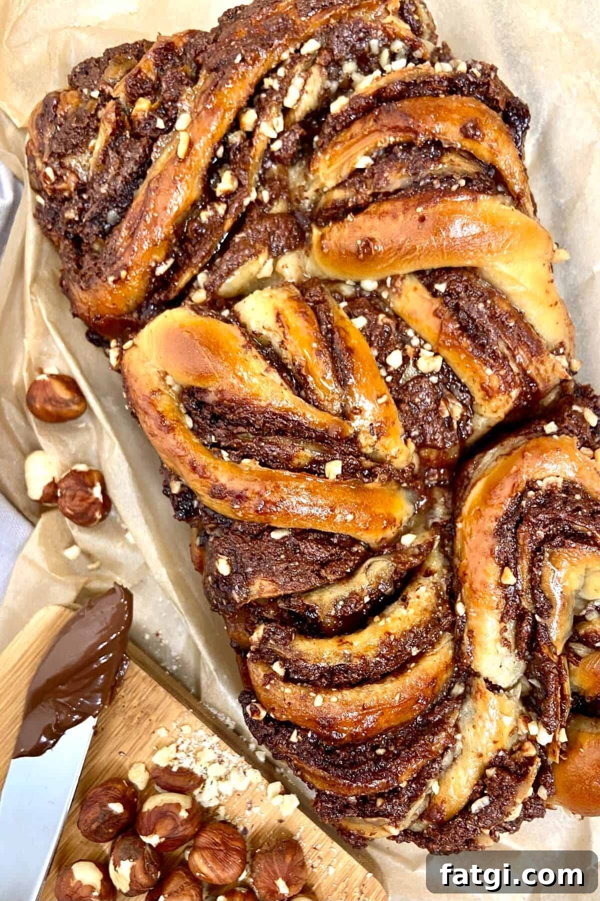 Whole babka, next to hazelnuts and Nutella spread on knife.