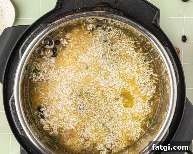 Overhead of the inside of an instant pot with white rice on top with a bit of chicken broth showing.