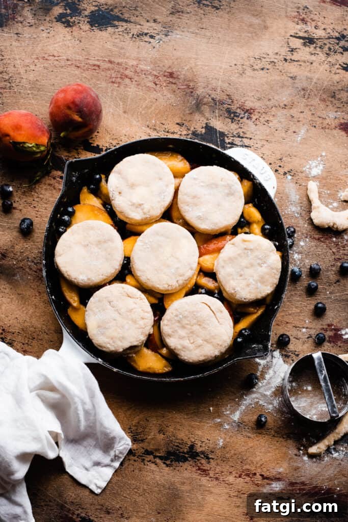 A cast iron skillet with blueberries and peach slices, topped with the unbaked biscuits.