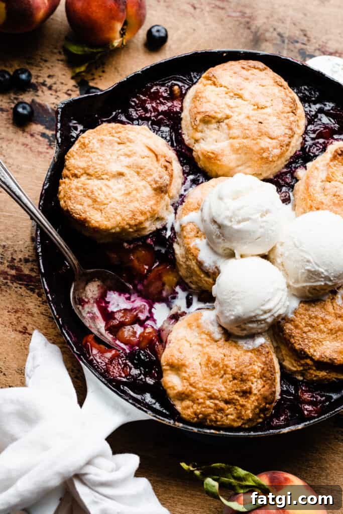 A close-up into the skillet of cobbler, with a spoon scooping up some of the fruit filling.