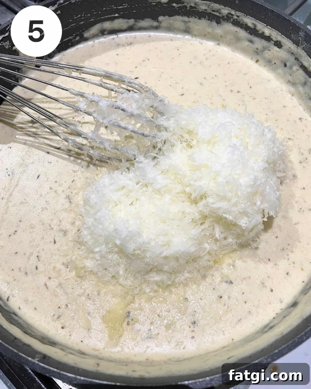 alfredo sauce in a pan with grated parmesan and asiago cheese on top.