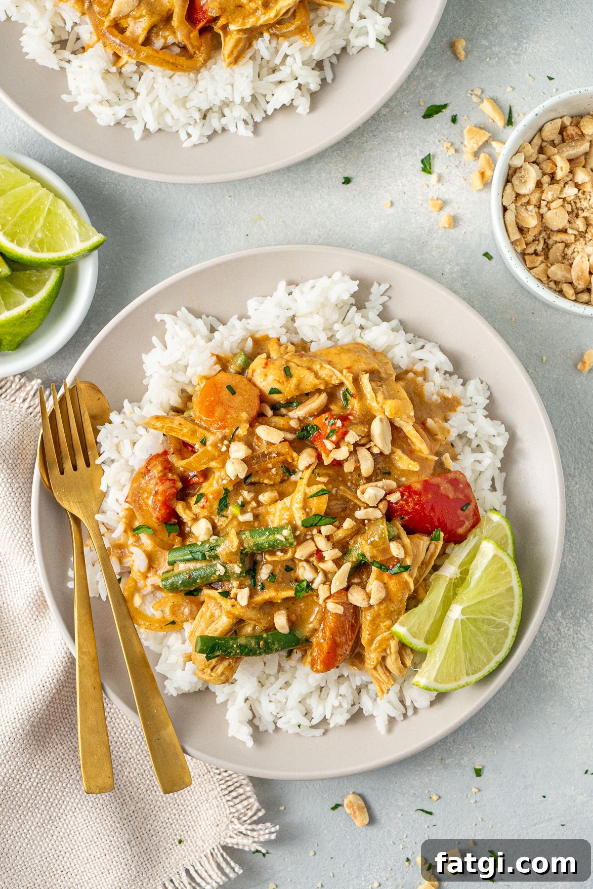 Slow cooker satay chicken served over rice with lime wedges and gold cutlery.