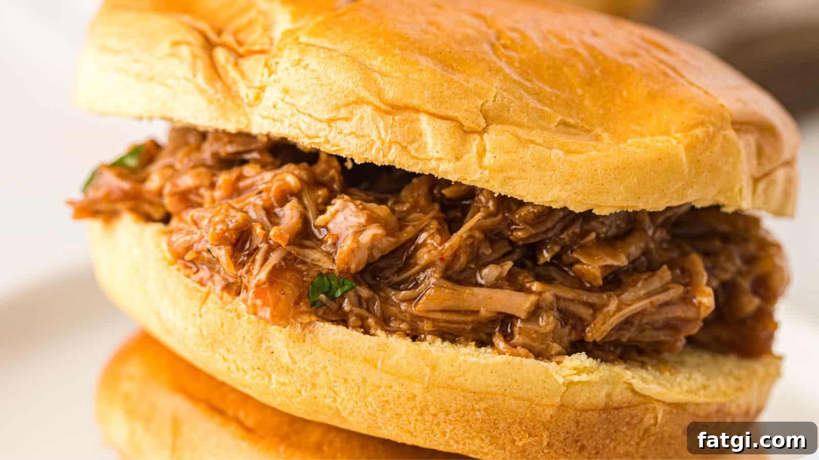 21 Pork Dinner Recipes for When You Need More on the Table 13 A close-up of a pulled pork sandwich on a soft bun, filled with shredded, saucy pork.