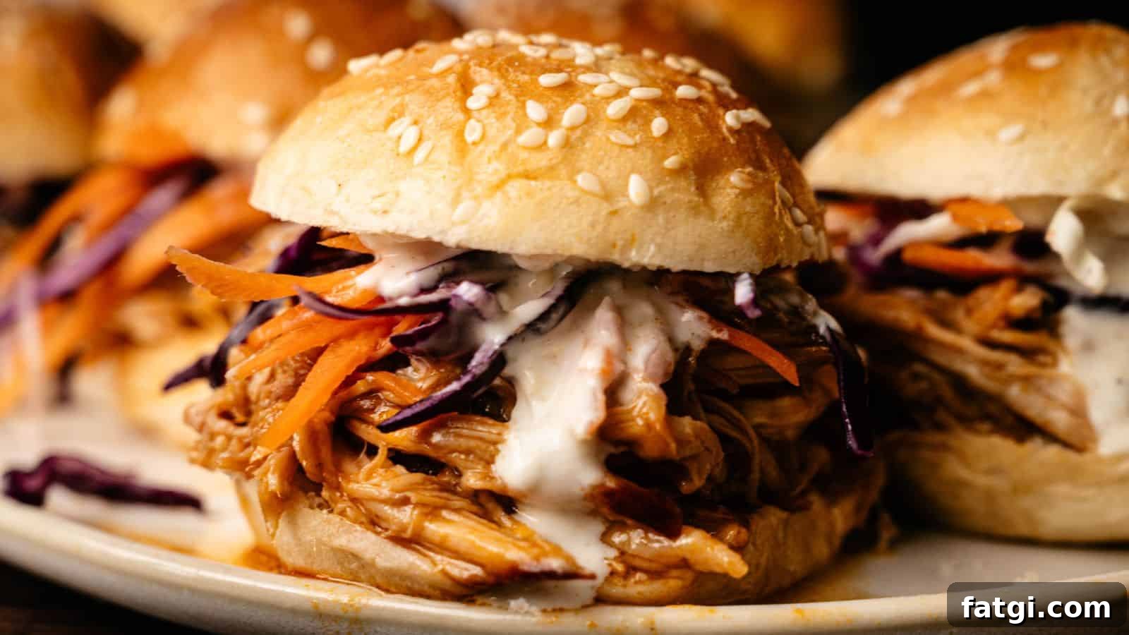 21 Pork Dinner Recipes for When You Need More on the Table 17 A close-up of a pulled chicken sandwich with sesame seed bun, shredded carrots, cabbage, and creamy sauce.