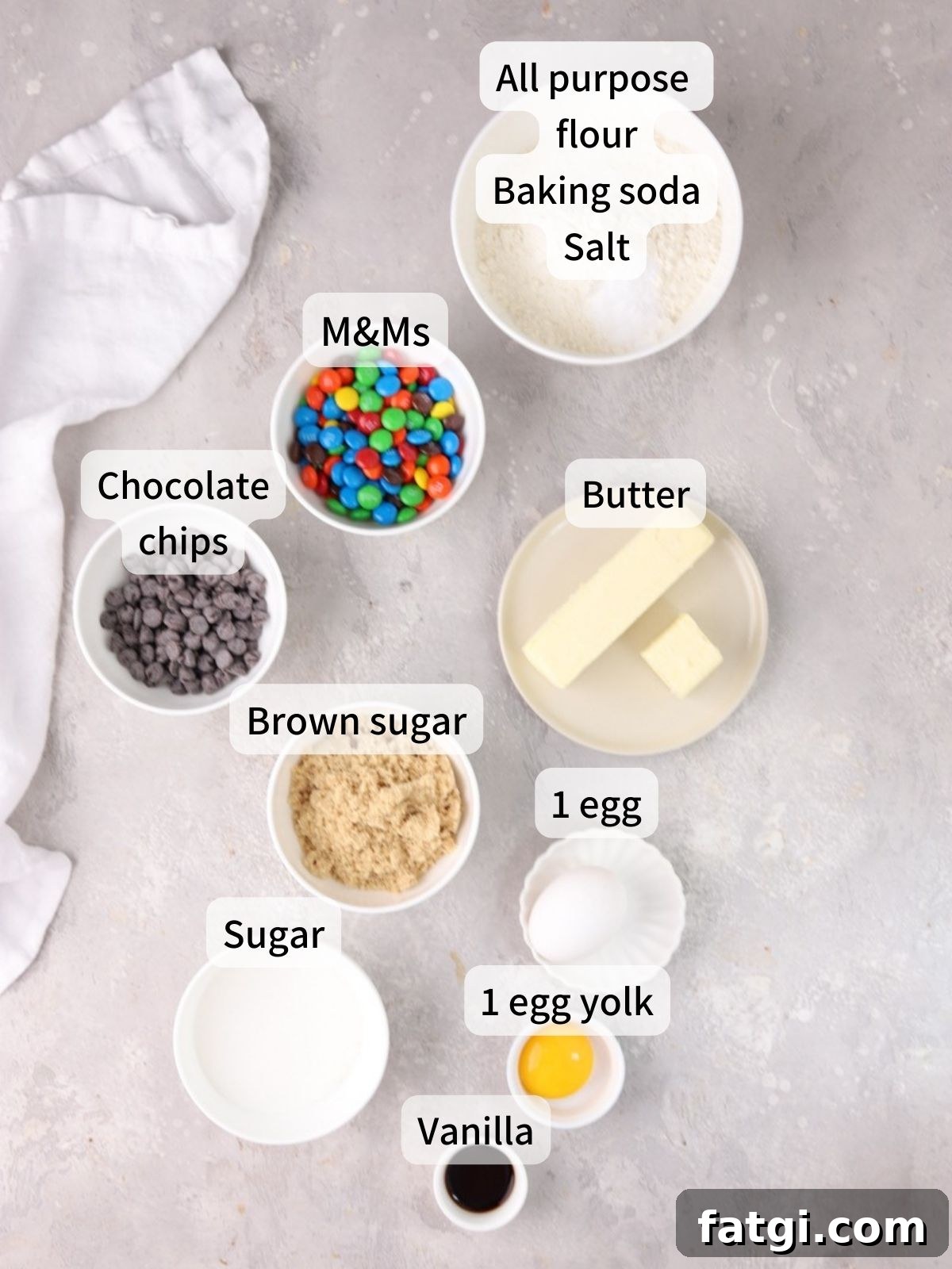Labeled ingredients needed to make M&M chocolate chip cookies laid out on a table.
