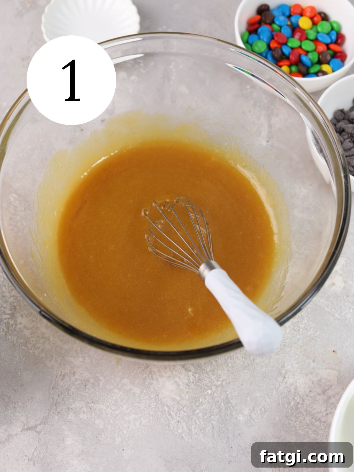 A glass mixing bowl with melted butter and sugars and a whisk.