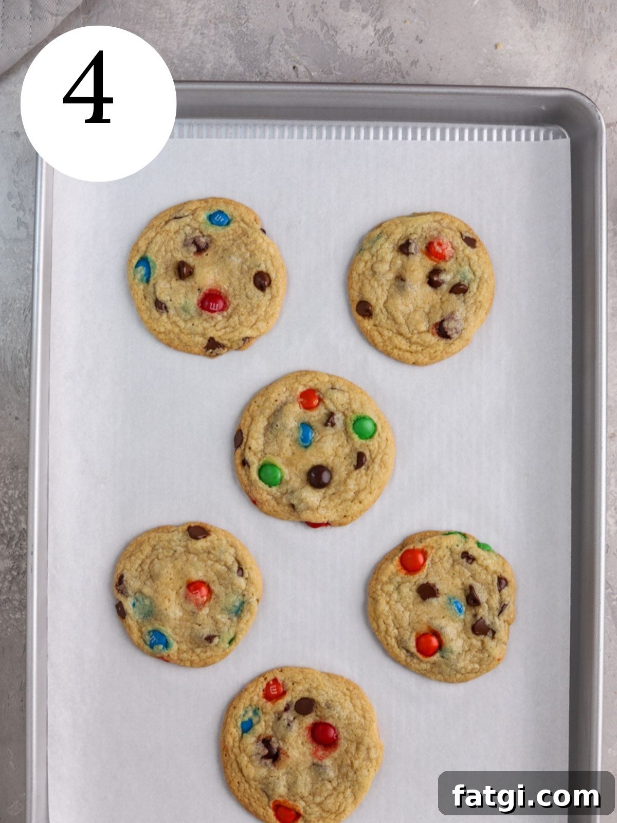 Chocolate chip cookies with M&Ms on a baking sheet lined with parchment paper.