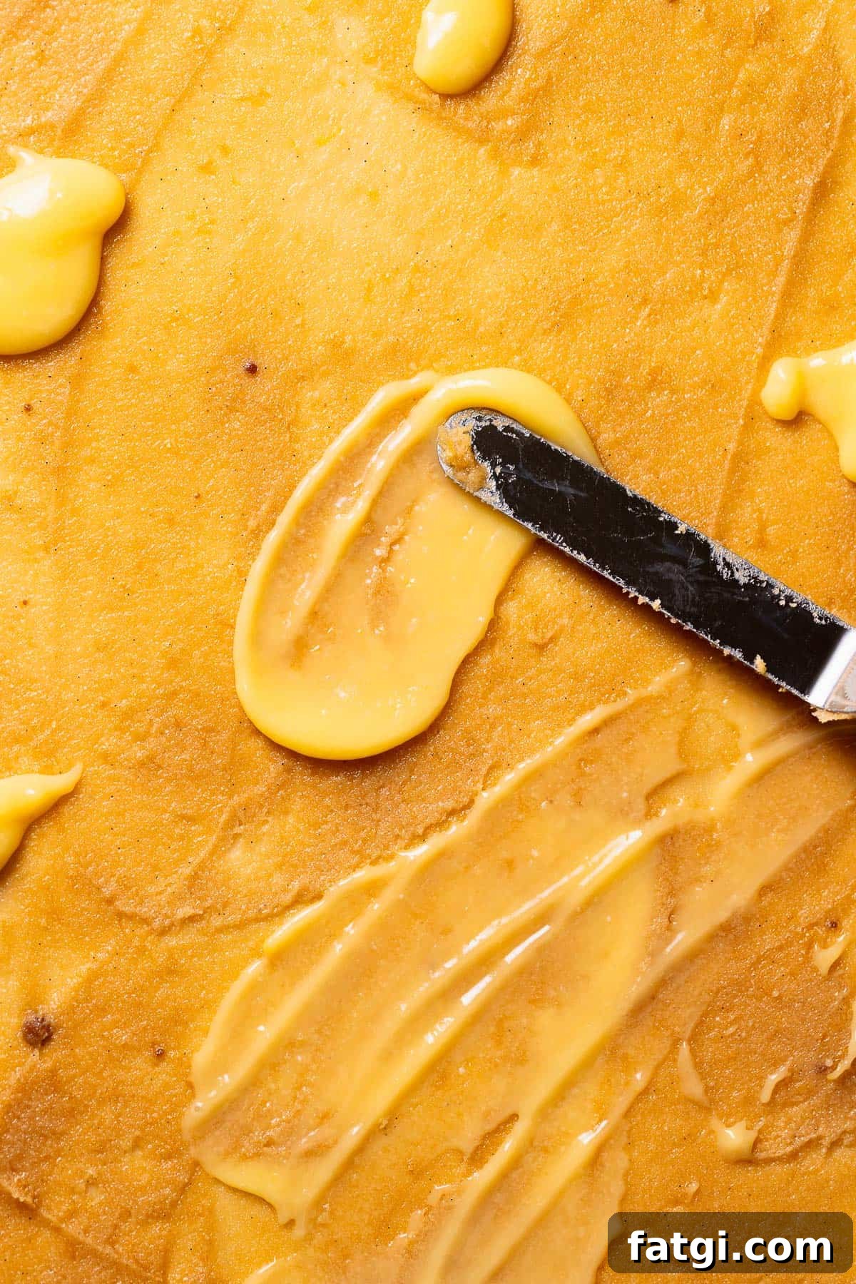 A spatula spreading the lemon filling and lemon curd across the rolled out dough.
