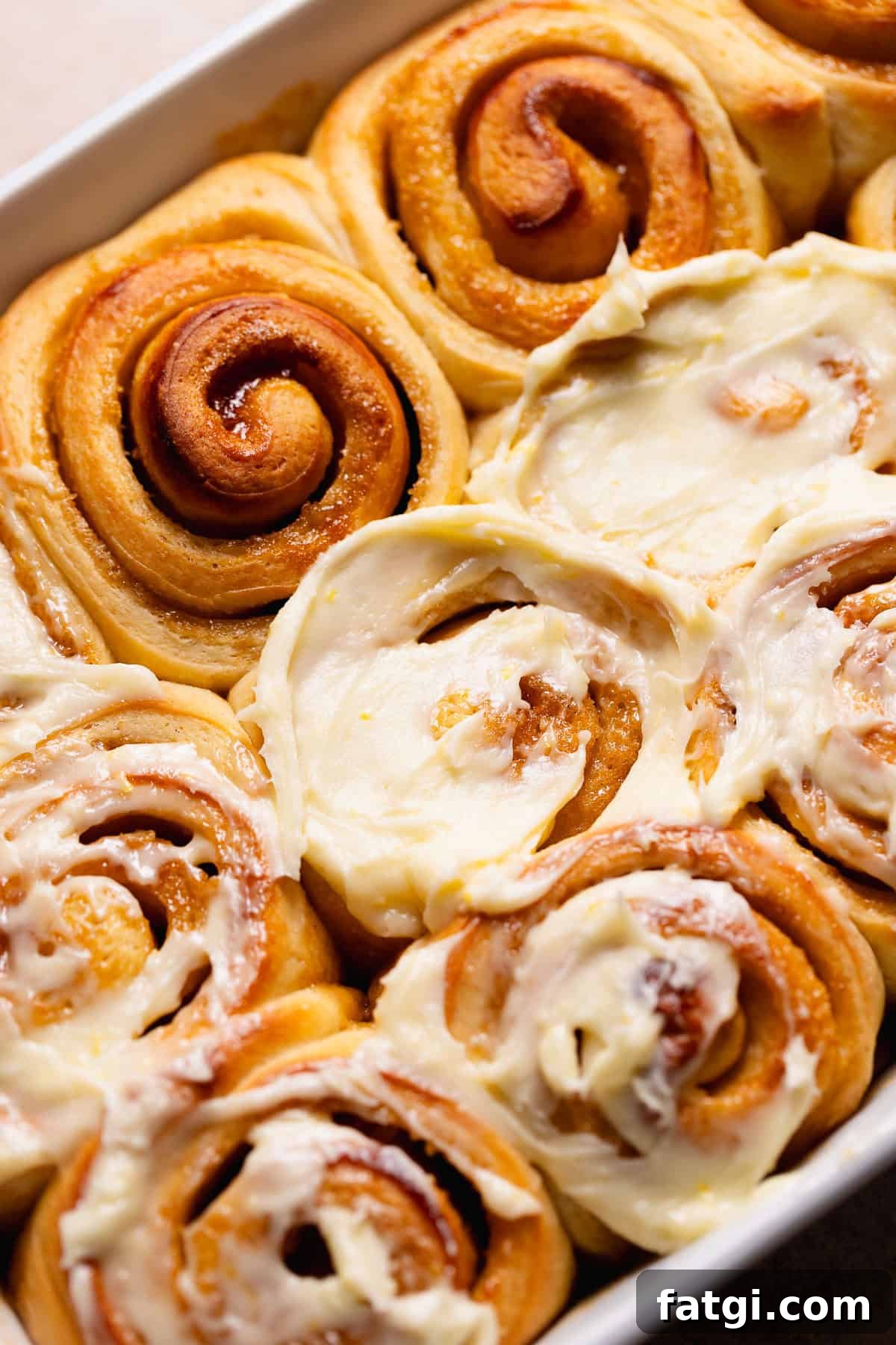Frosting the tops of the baked rolls with cream cheese frosting.