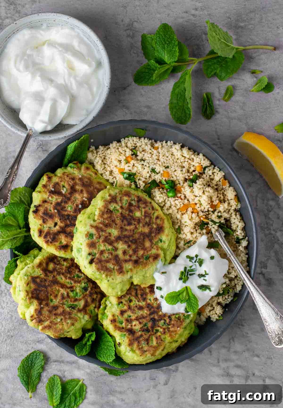 Cheesy Green Pea Fritters Recipe 2 Four pea fritters in a bowl with a portion of couscous and a dollop of Greek yoghurt.