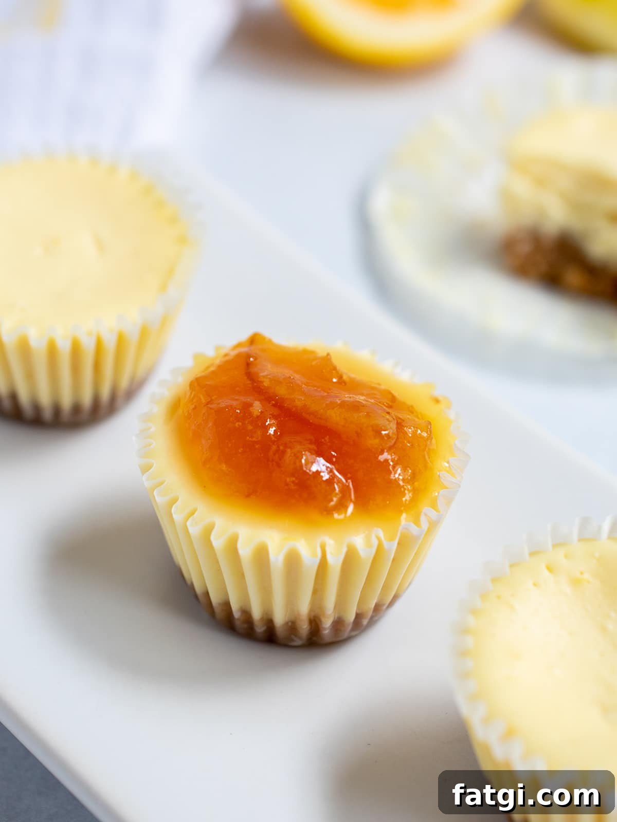 Three mini cheesecake bites on a white plate with jam on the middle one.