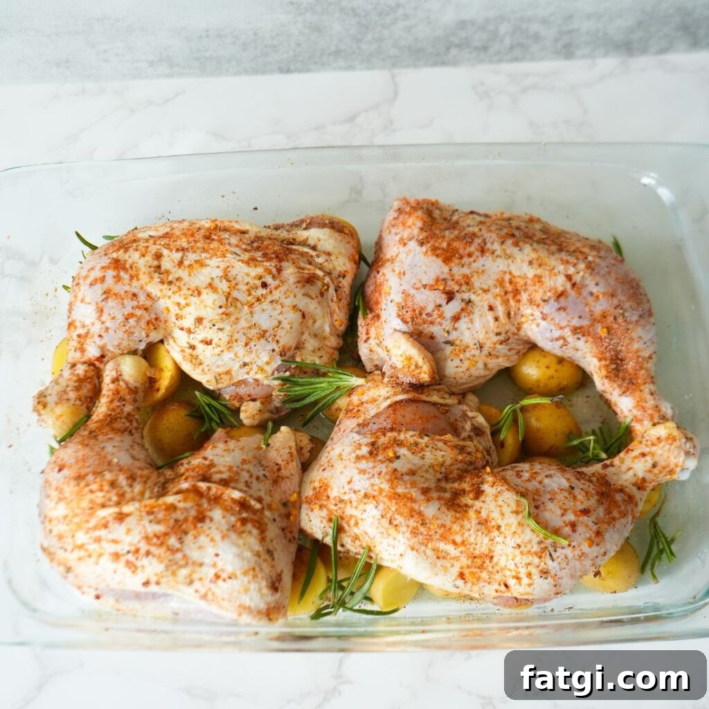 Chicken leg quarters with seasoning rub on top of baby potatoes garnished with rosemary.