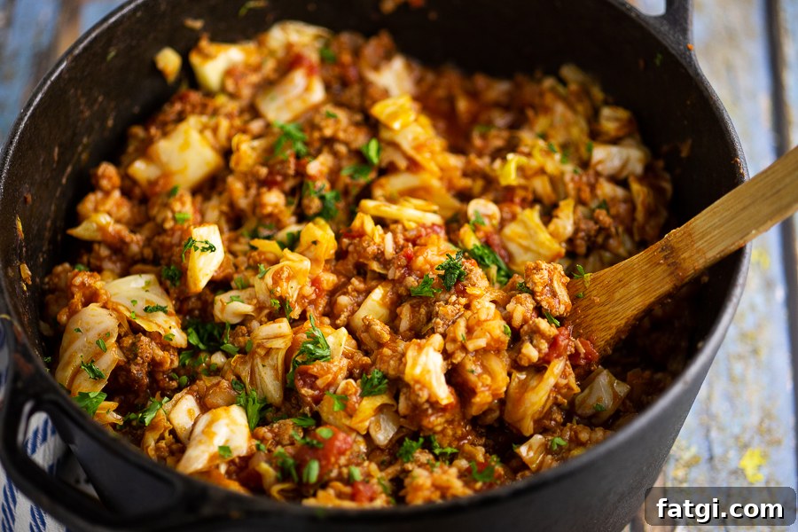Unstuffed cabbage rolls in a black cast iron Dutch oven with a wooden spoon in the middle on a rustic wood background.