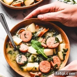 Hands picking up a bowl of potato soup with kale and sausages.