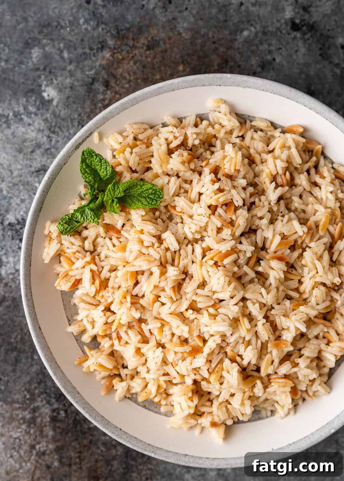 overhead: a serving bowl full of orzo rice with fresh mint sprigs as a garnsih