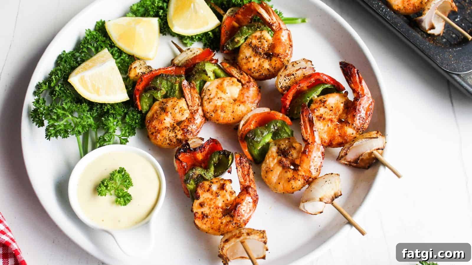 Grilled shrimp skewers with red and green bell peppers, served with lemon wedges and a dipping sauce on a white plate.
