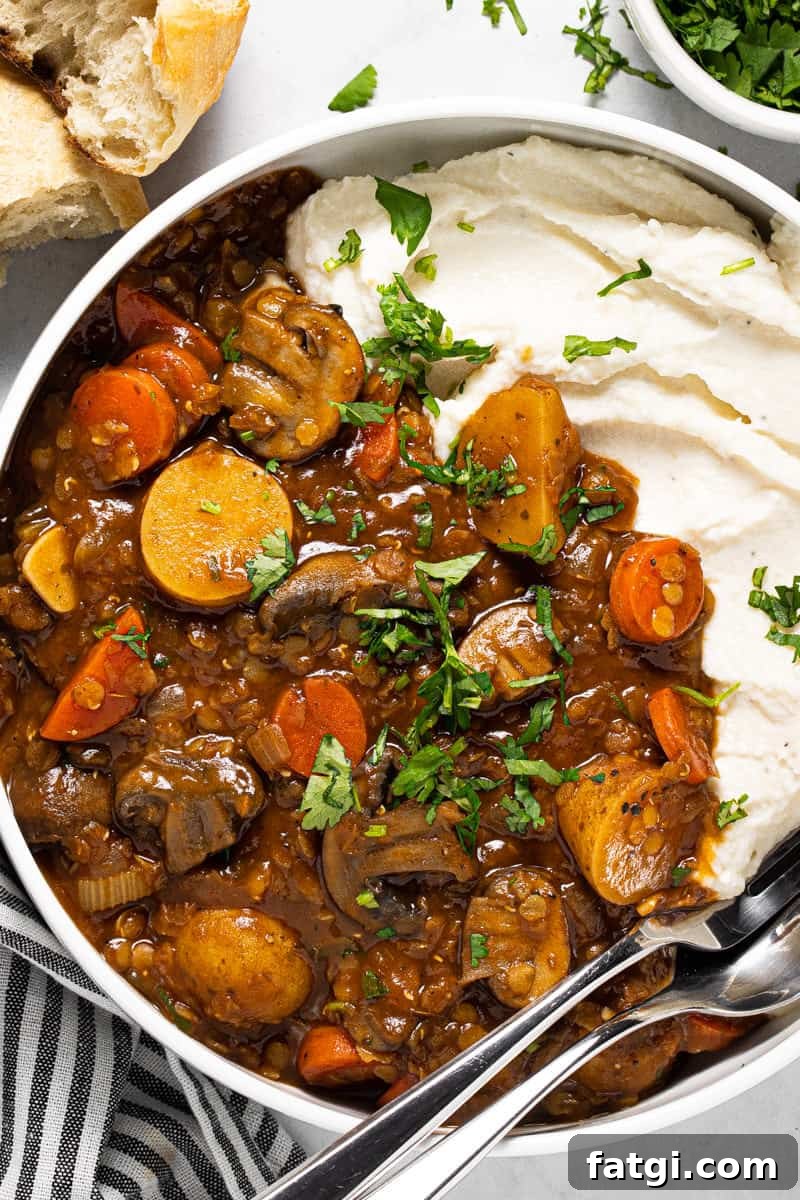 Large white bowl filled with vegetable stew recipe and mashed potatoes garnished with fresh parsley 