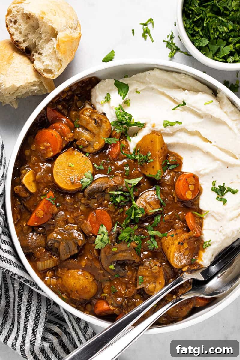 Large white bowl filled with vegetable stew recipe and mashed potatoes garnished with fresh parsley 