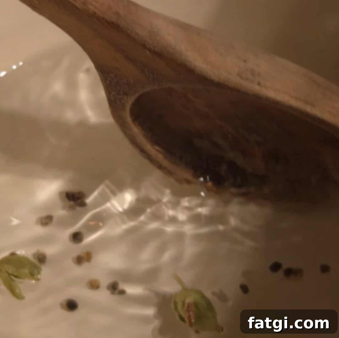 Homemade Cardamom Syrup Recipe for Coffee and Cocktails 7 Stirring crushed cardamom pods in water inside a white saucepan to start the cardamom syrup base.