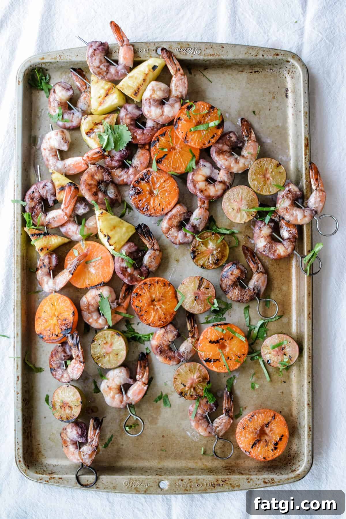 Grilled Shrimp Skewers with Sangria Marinade 3 An overhead image of grilled shrimp skewers on metal skewers with shrimp, tangerine halves, pineapple, and key lime halves.