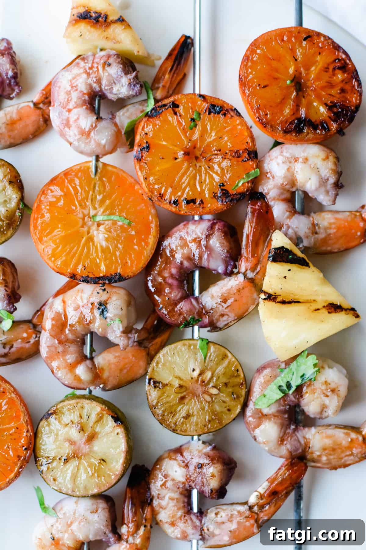 Grilled Shrimp Skewers with Sangria Marinade 4 An overhead image of grilled shrimp, grilled tangerine halves, pineapple, and grilled key limes skewered on metal skewers.