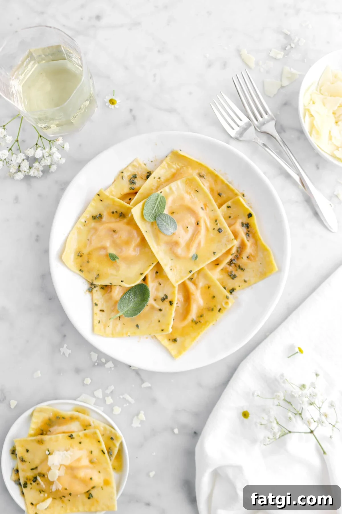 ravioli in white plate with three sage leaves on top with two forks beside and glass of wine beside.