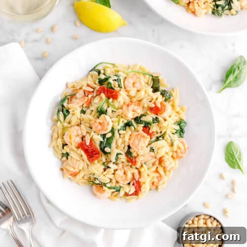 shrimp orzo in plate with forks, spinach leaves, pine nuts, and lemon wedges around