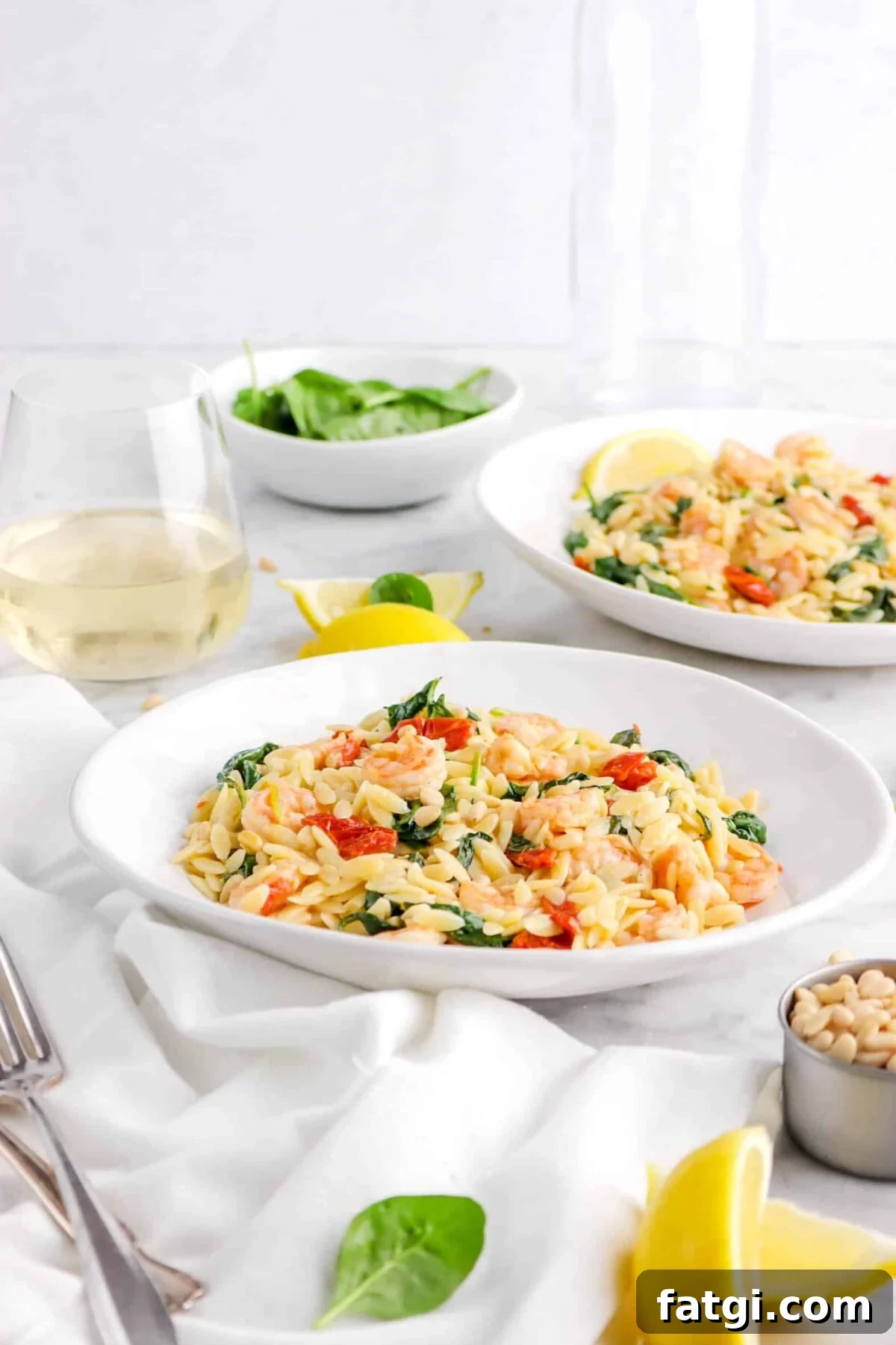 two bowls of orzo with shrimp, sun-dried tomatoes, lemon wedges, and glass of white wine