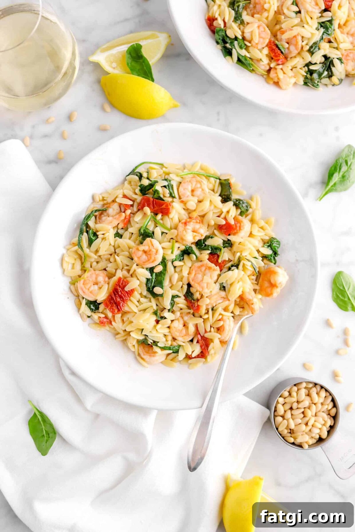 fork inside shrimp orzo with glass of white wine, lemon wedges, and spinach leaves