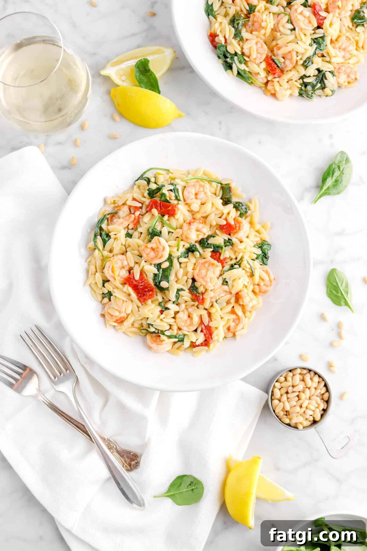 shrimp orzo and spinach in two plates with lemon, spinach leaves, and pine nuts around