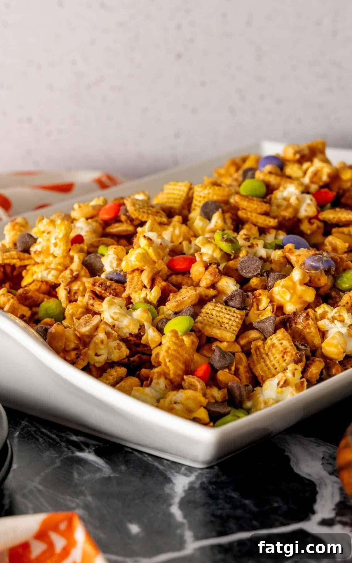 A large white serving platter of monster munch made up of popcorn, M&M's, chocolate morsels, and peanuts.