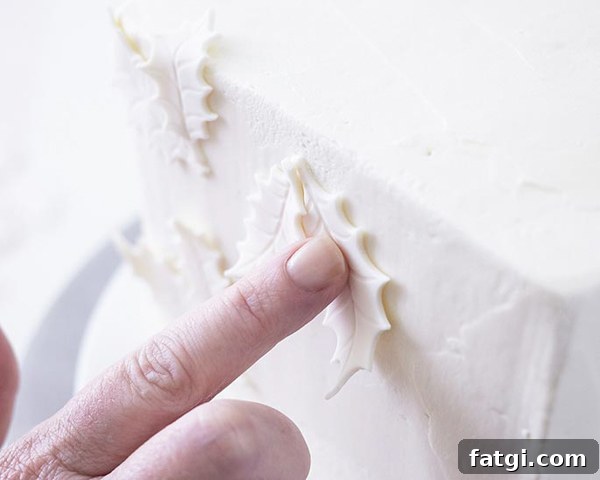 Applying white fondant holly leaves to cake side