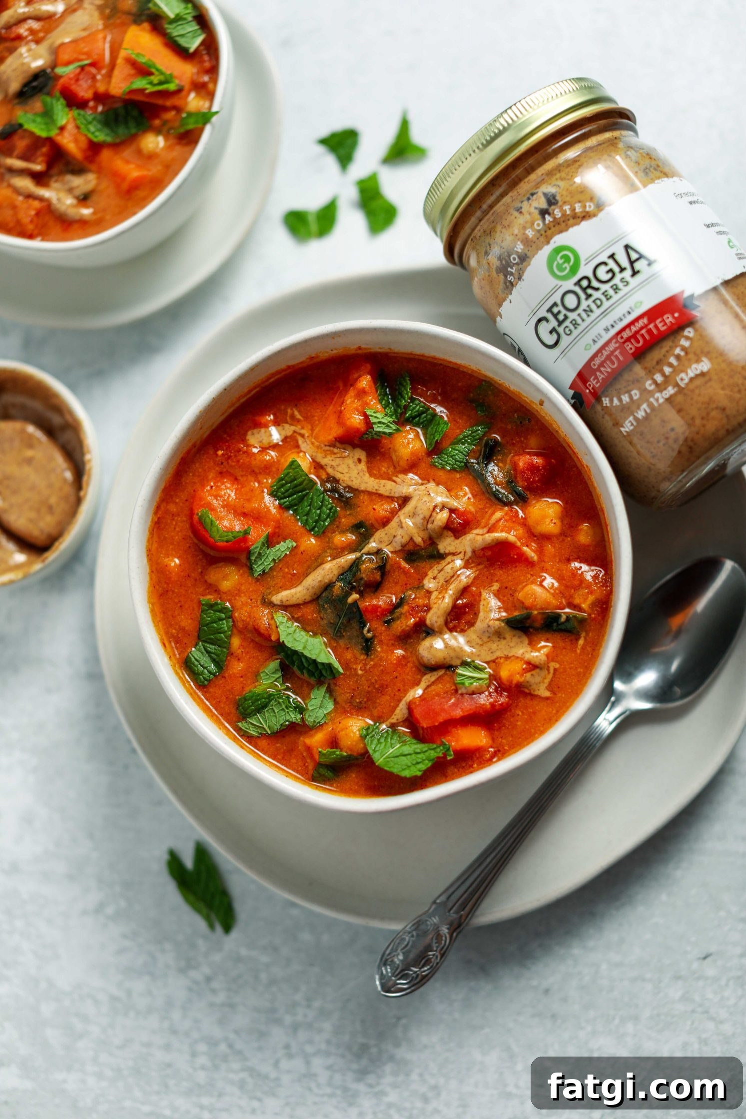 Authentic West African Peanut Stew Recipe 5 African Peanut Butter Stew served in a bowl on a plate with a spoon and fresh mint on top by Flora & Vino