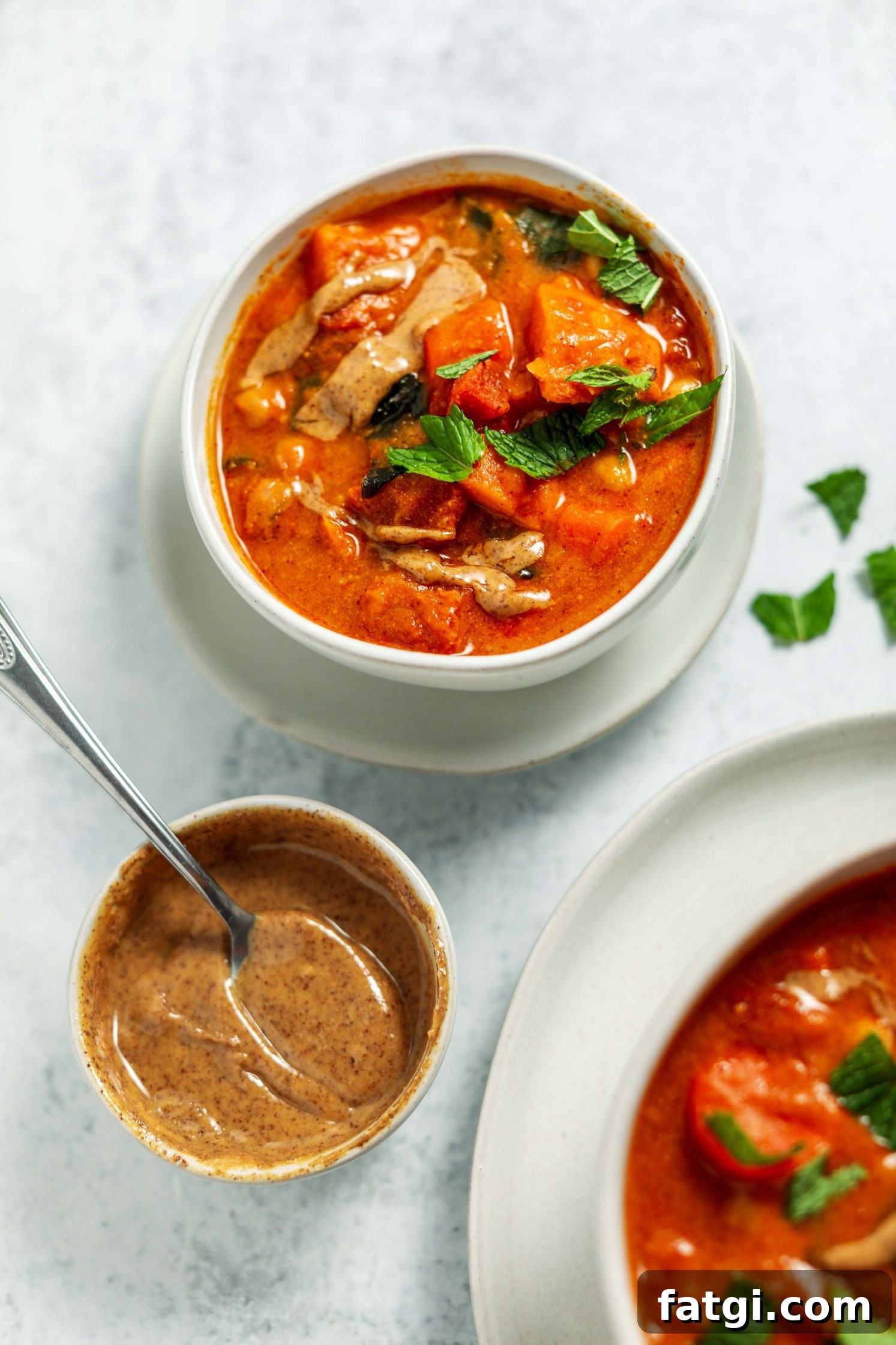 Authentic West African Peanut Stew Recipe 7 African Peanut Butter Stew served in a bowl on a plate with a spoon and fresh mint on top by Flora & Vino