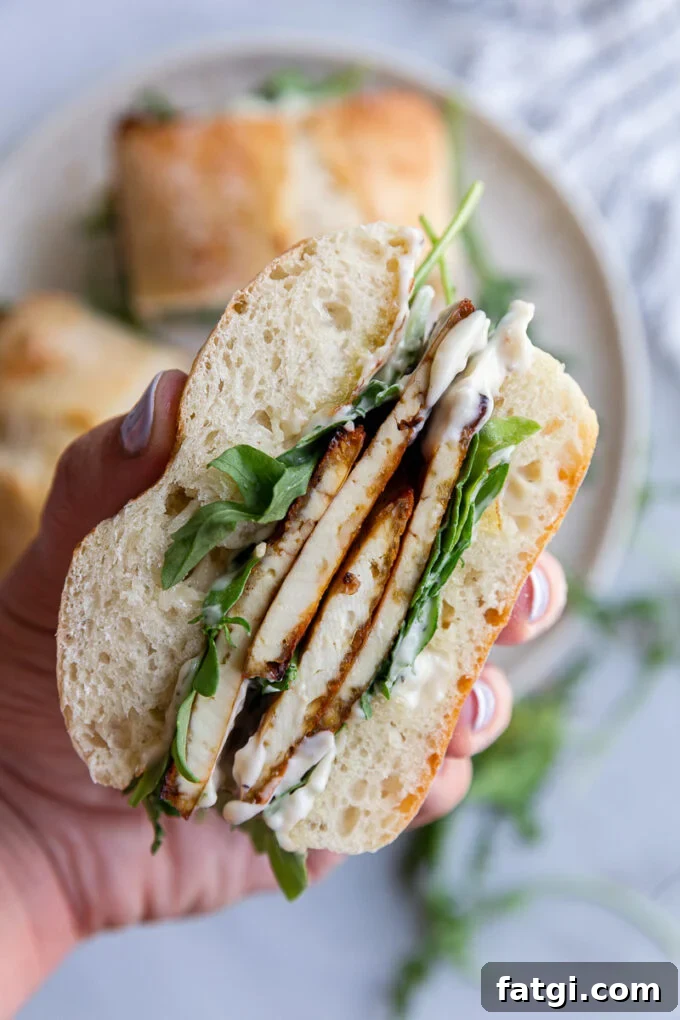 Hand holding a sandwich with tofu and lettuce.