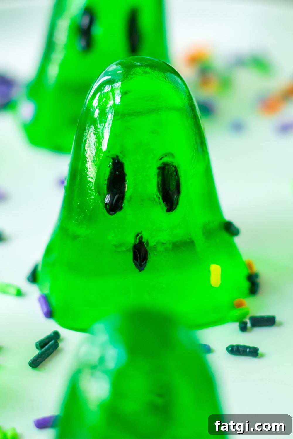Ghost Jello Shots for Halloween Parties 8 close up of a green ghost jello shot on plate with Halloween sprinkles around it