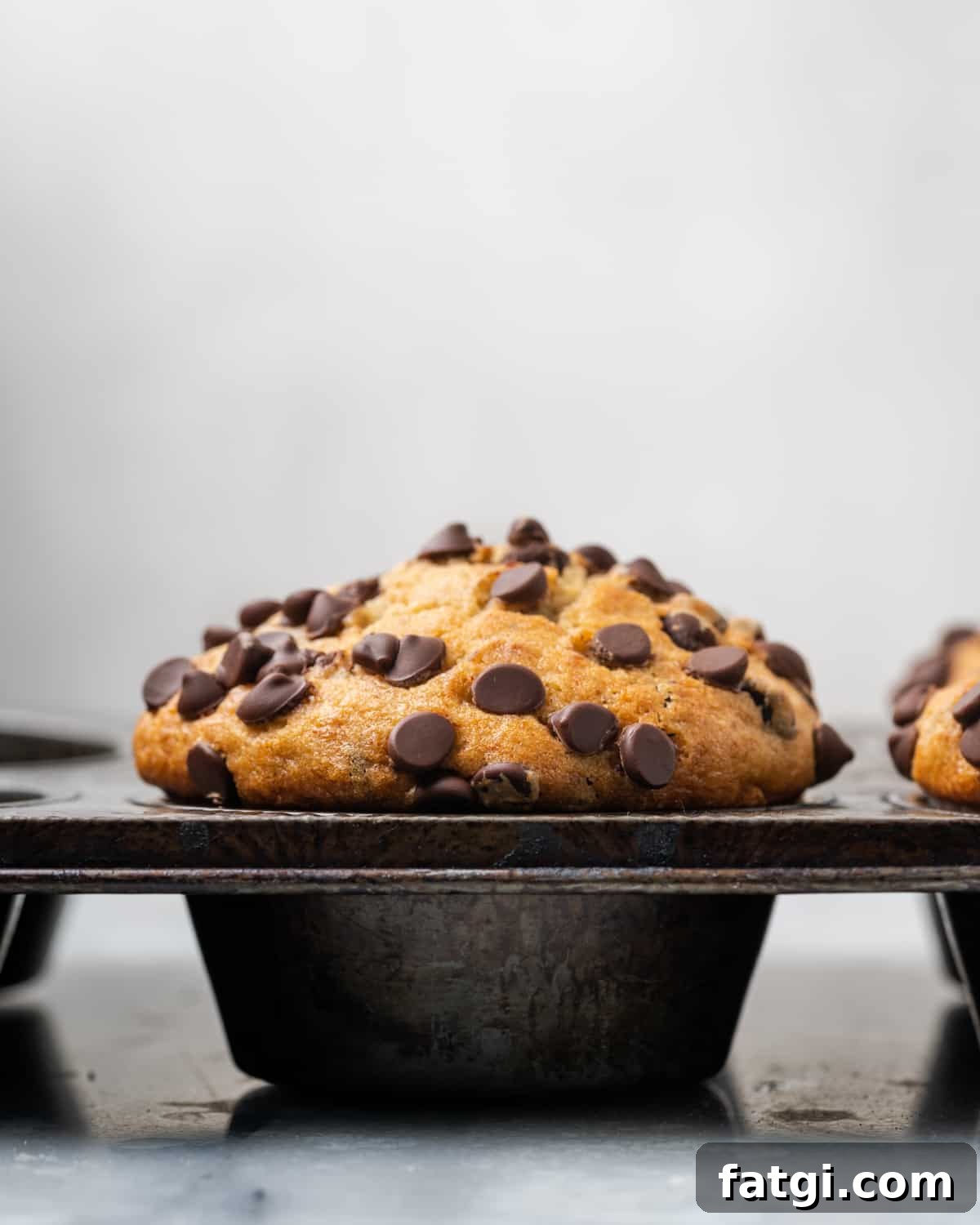 A batch of freshly baked gluten free banana chocolate chip muffins in the muffin tin showing the tall domed tops.