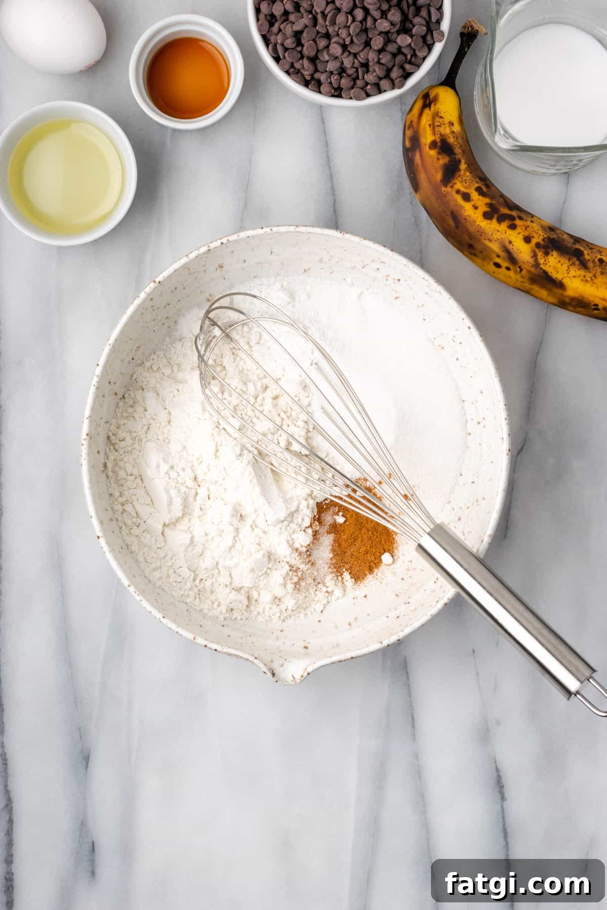 Gluten free flour, sugar, baking powder and spices being whisked together in a large white mixing bowl.