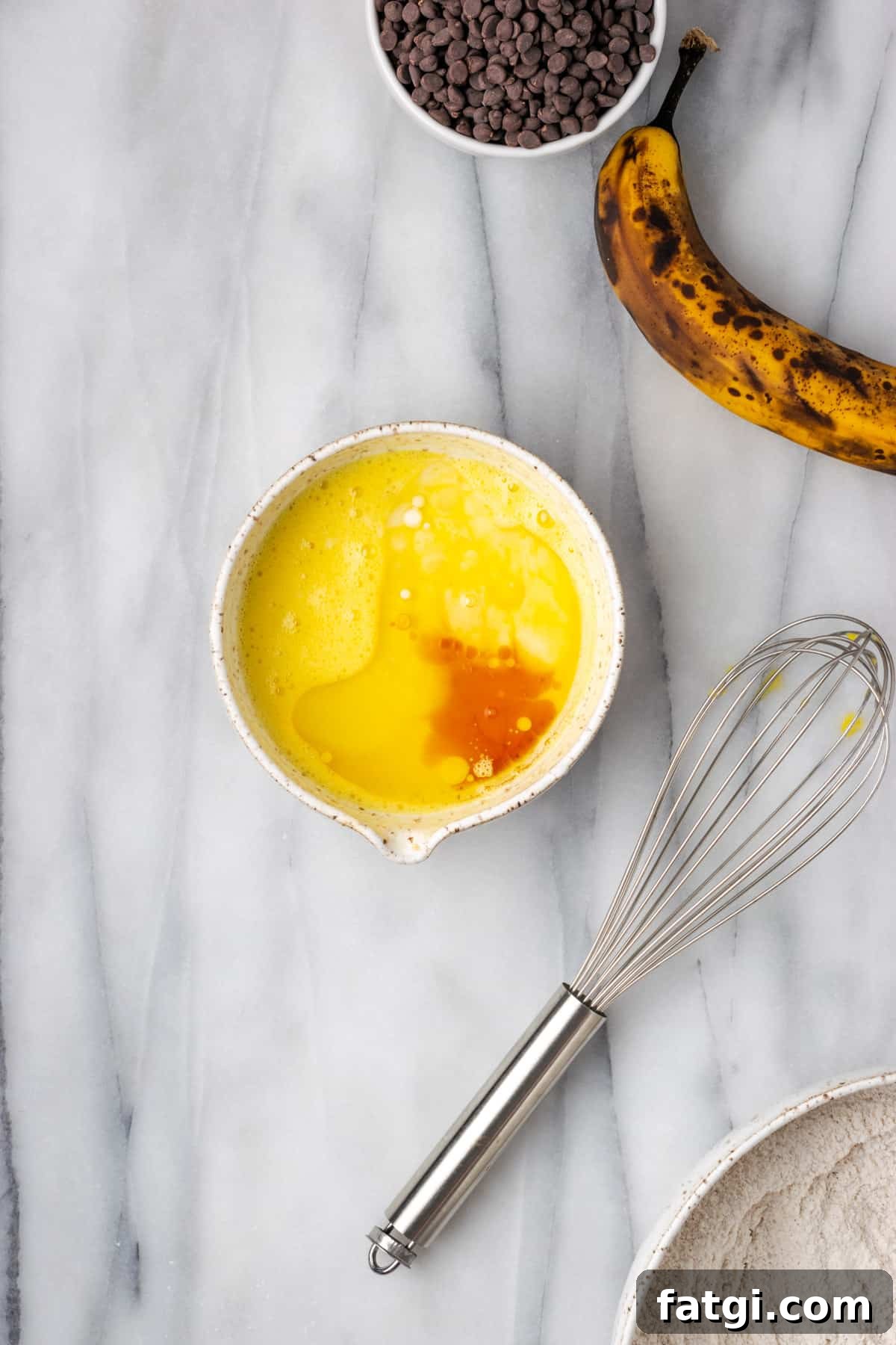 Oil, vanilla and milk added to the beaten egg in a small white bowl.
