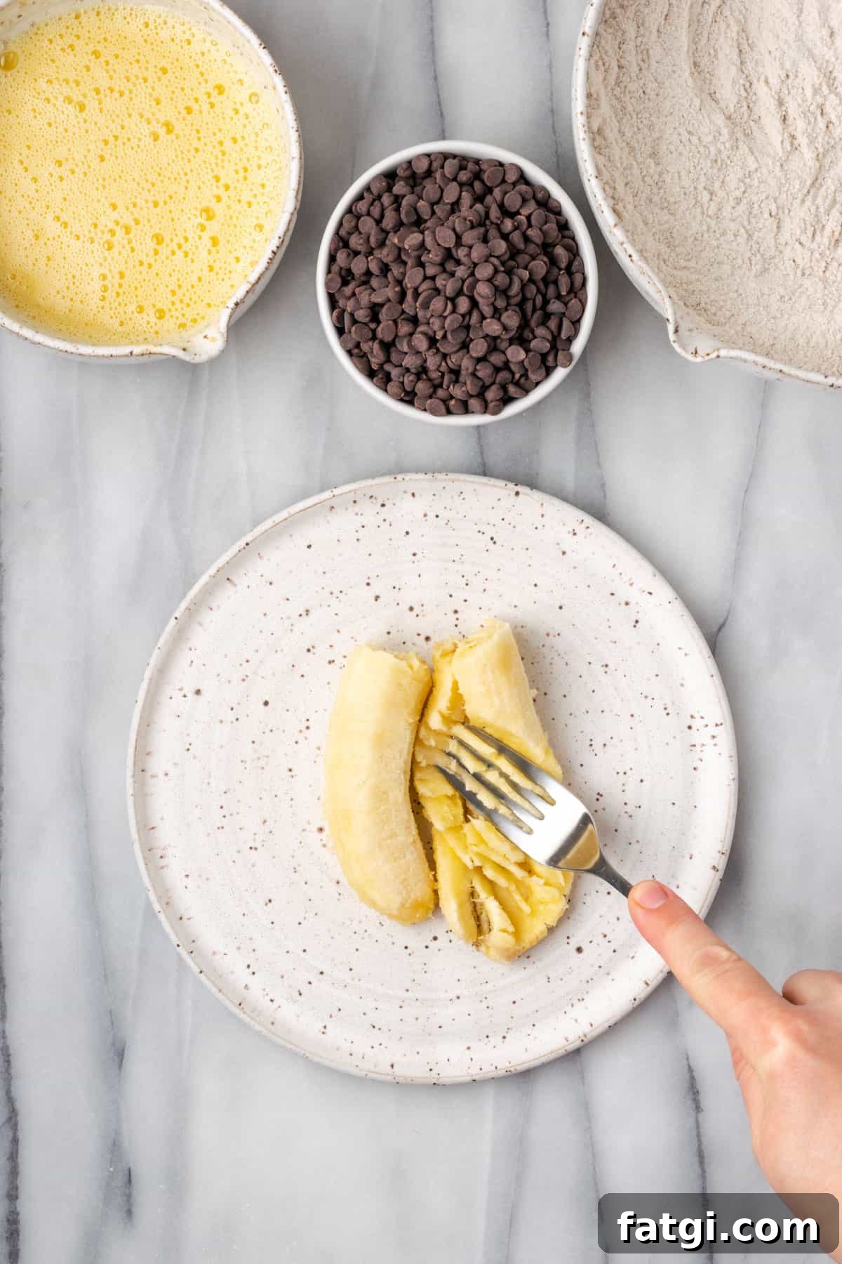 A banana being mashed on a plate with the tines of a fork.