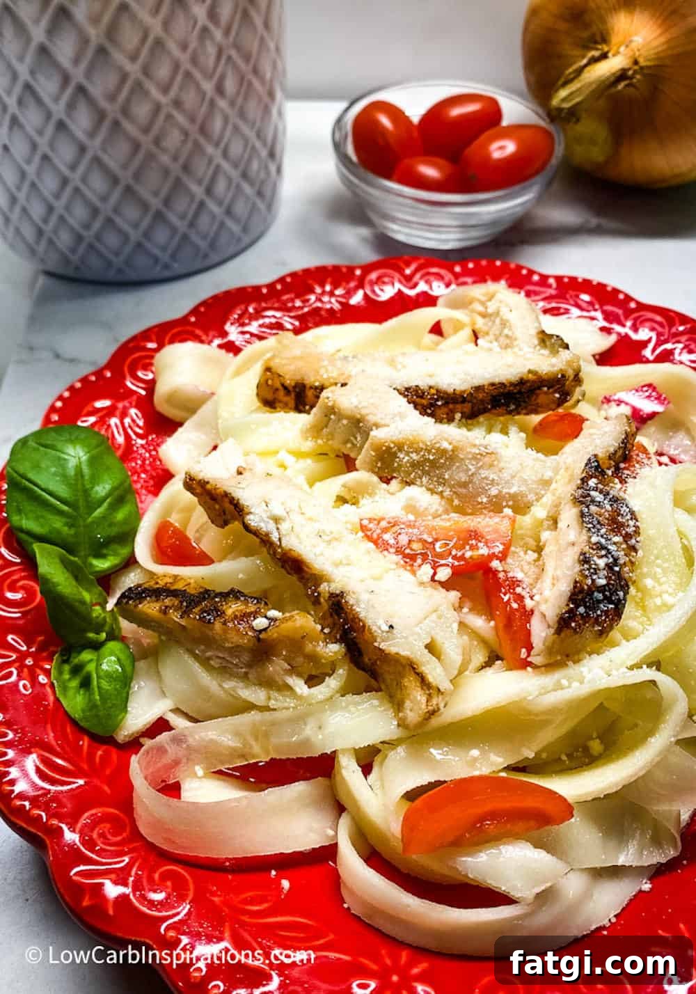 Keto pasta noodles served with chicken, tomatoes and basil served on a red plate.
