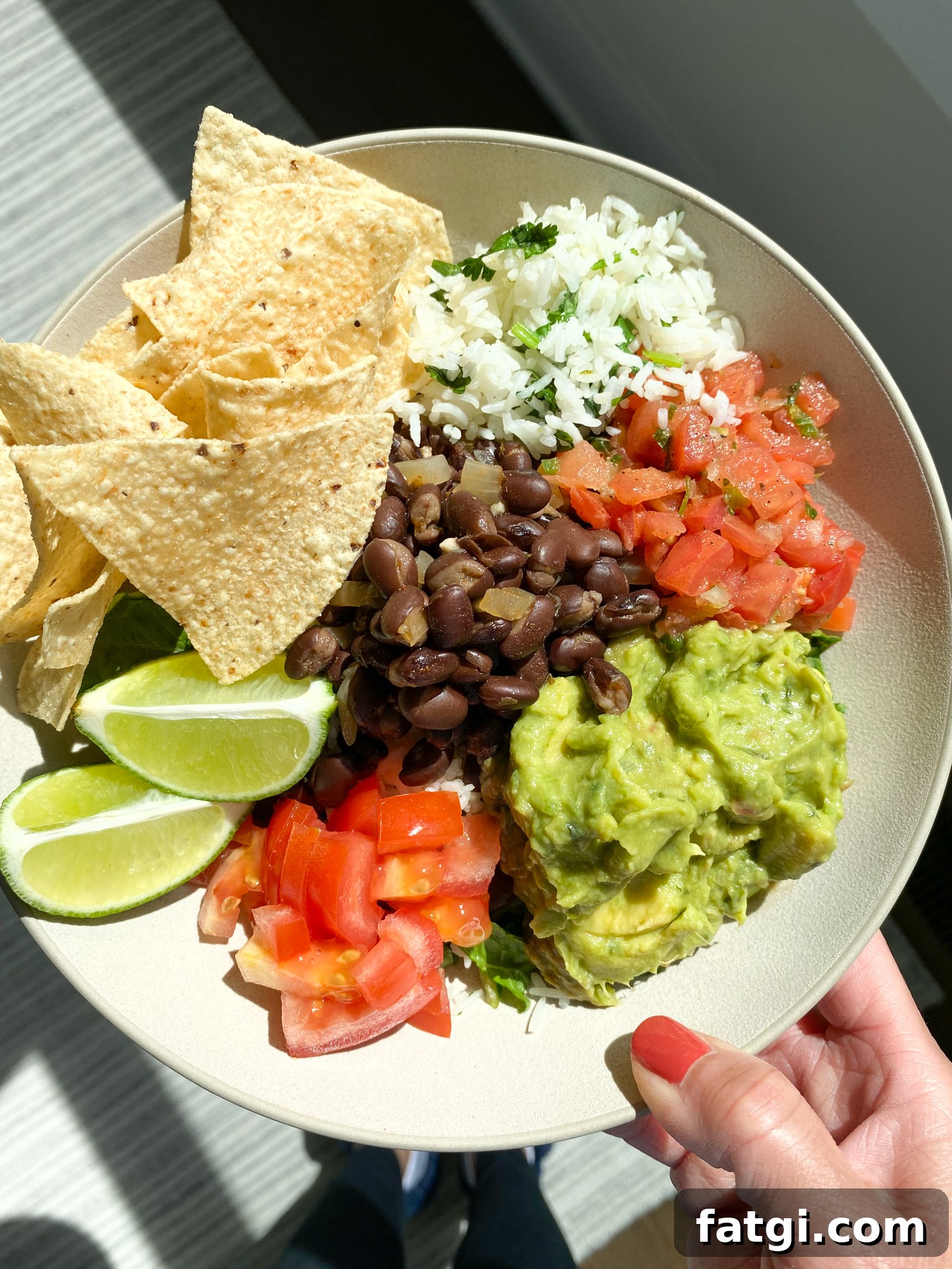 Chipotle style salad bowl with cilantro lime rice, romaine lettuce, black beans, guacamole, pico de gallo, tomatoes, lime, and tortilla chips
