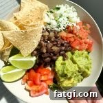 Chipotle style salad bowl with cilantro lime rice, shredded romaine lettuce, black beans, guacamole, pico de gallo, tortilla chips, and lime