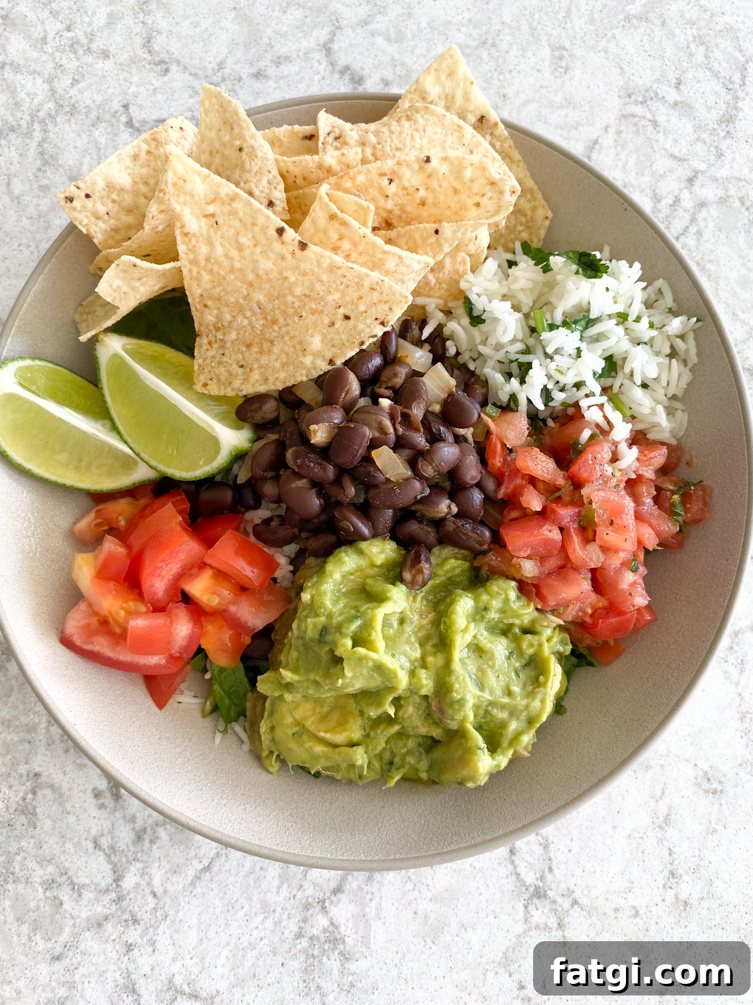Finished Chipotle style salad bowl served with cilantro lime rice, black beans, guacamole, pico de gallo, tomatoes, lime wedges, and tortilla chips
