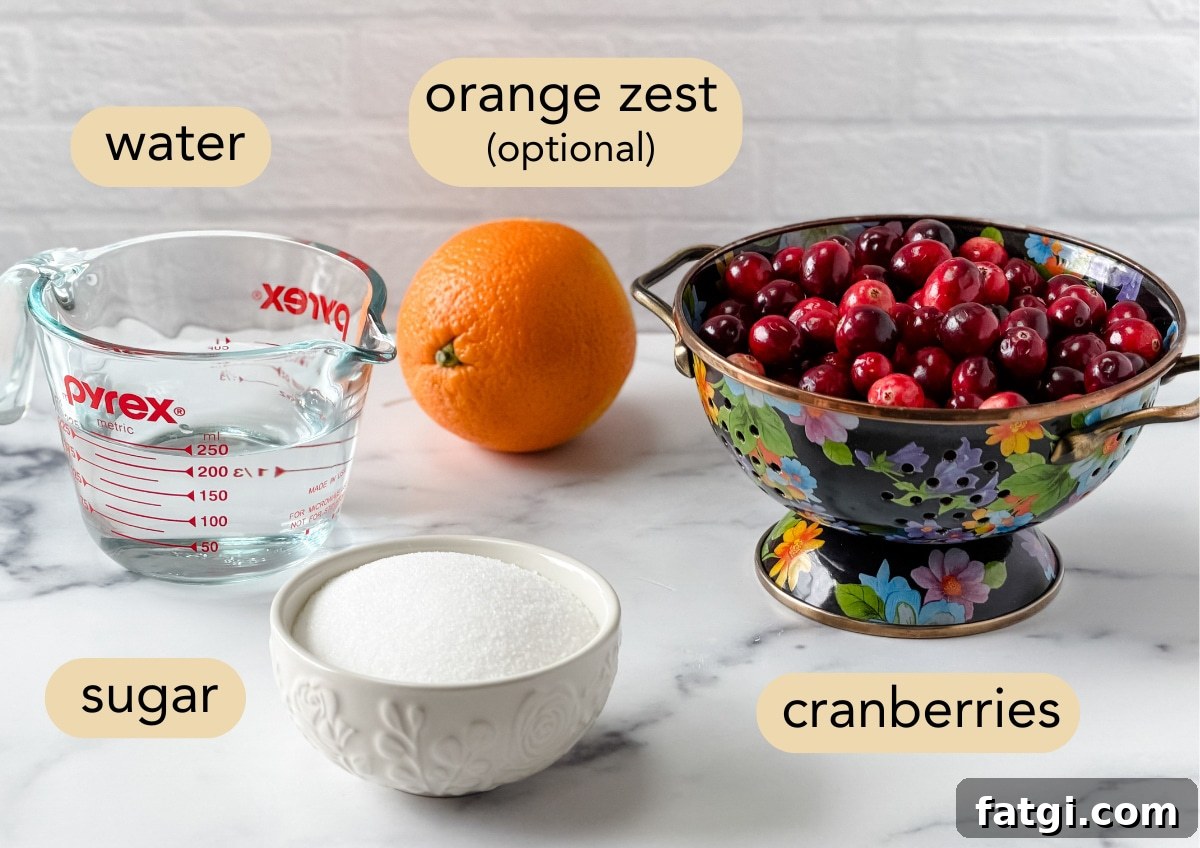 Overhead view of ingredients for homemade cranberry sauce: measuring cup of water, orange for zest, fresh cranberries, and a bowl of sugar.