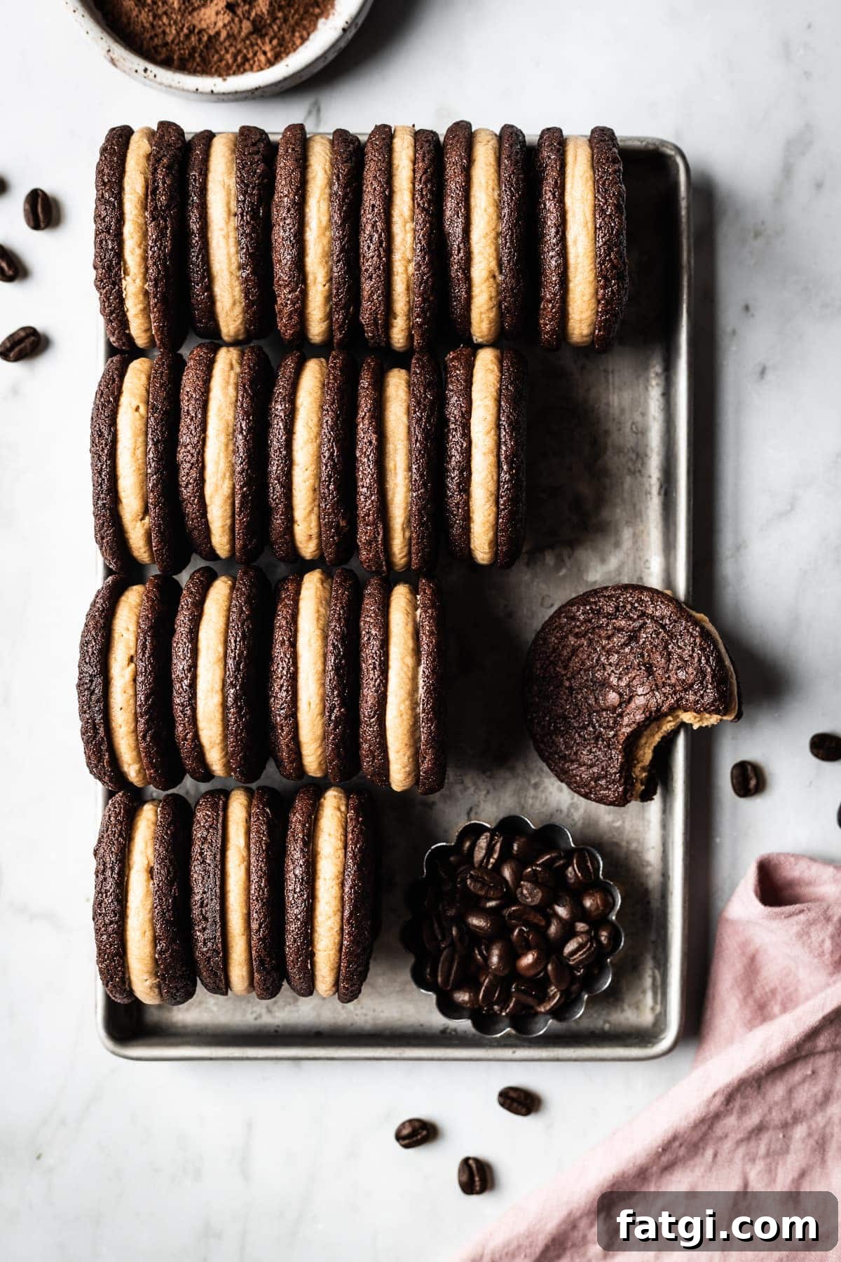 Four rows of sandwich cookies filled with frosting on a small metal pan.
