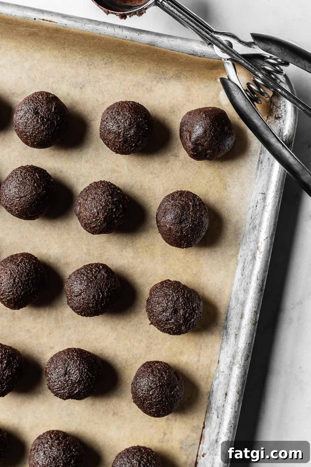 Rolled balls of chocolate mascarpone cookie dough on a parchment lined baking sheet.