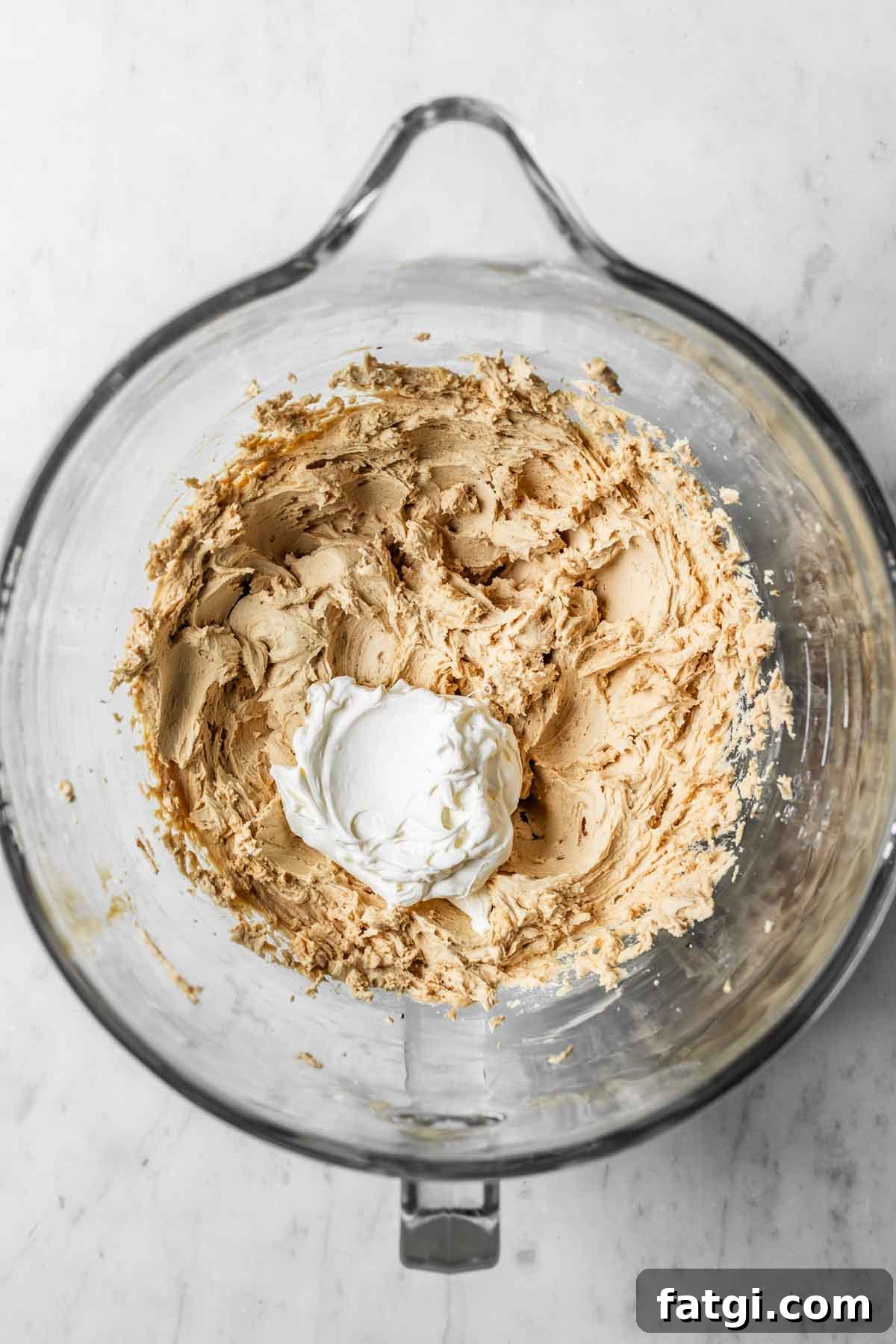 Mascarpone added to coffee buttercream frosting in a glass mixing bowl.