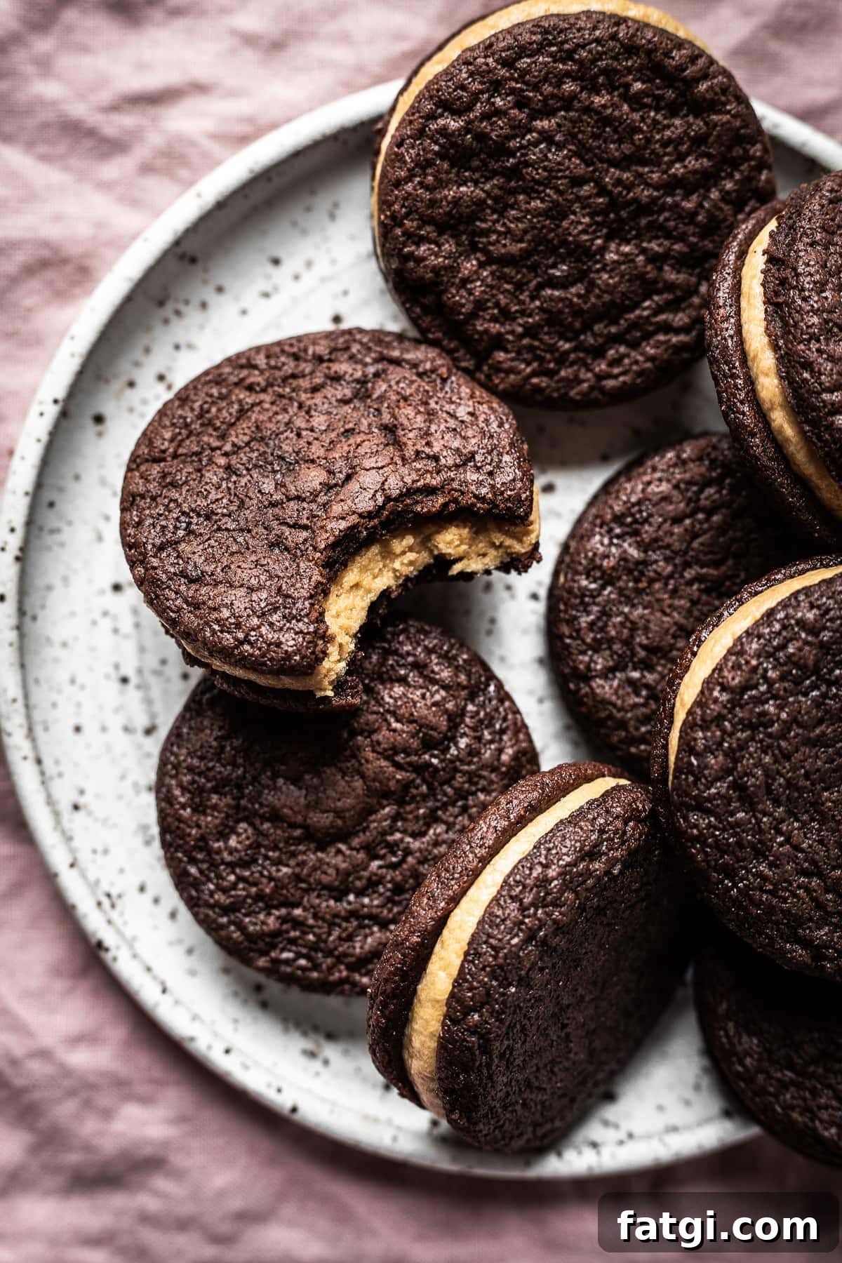 Chocolate coffee mascarpone sandwich cookies on a plate. One cookie has a bite missing.